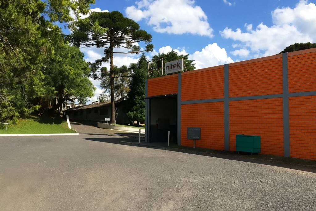 Vista da sede da Nitek com área externa arborizada e prédio industrial em tijolos laranja
