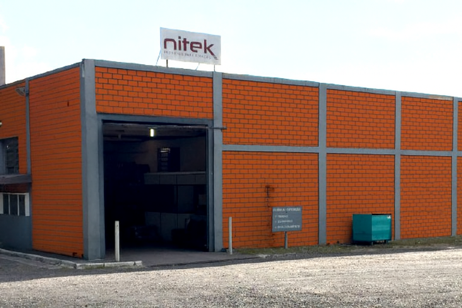 Fachada da empresa Nitek com estrutura industrial em tijolos laranja e placa identificando a marca